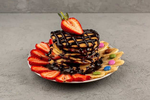 front view pancakes with sliced red strawberries and bananas along with chocolate inside plate on the light floor