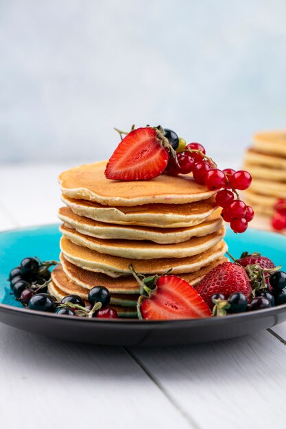 Front view pancakes with strawberries black and red currants on a plate