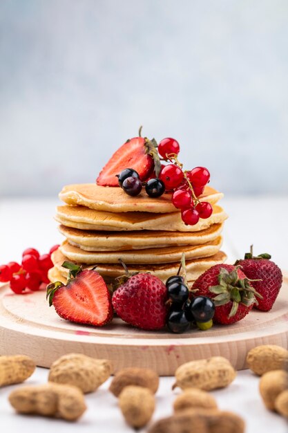 Front view pancakes with strawberries black and red currants on a tray with peanuts