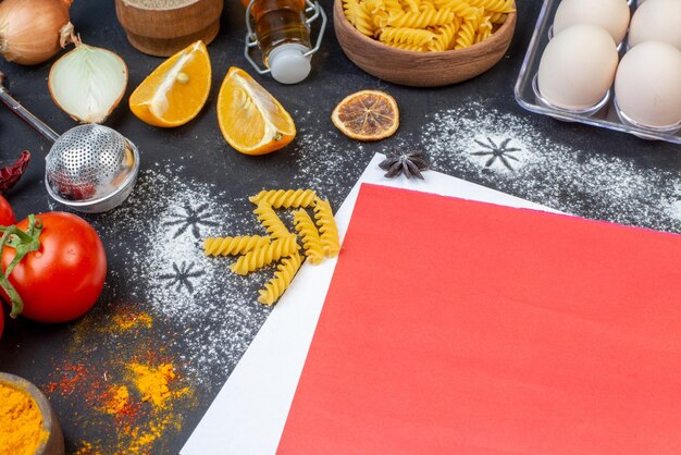 Front view paper blanks with eggs vegetables raw pasta and seasonings on a dark background dough vegetable egg meal salad food color