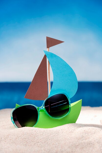 Вид спереди бумажный кораблик на песчаном пляже с очками