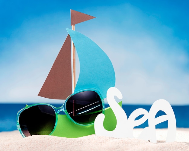 Front view of paper boat on beach with sunglasses