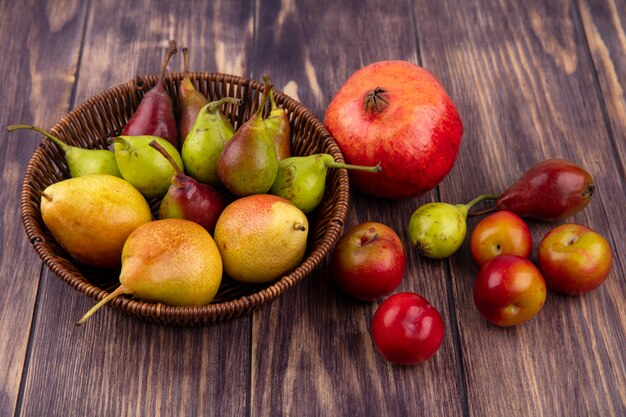 Front view of peaches in basket with pomegranate peach plum on wooden surface