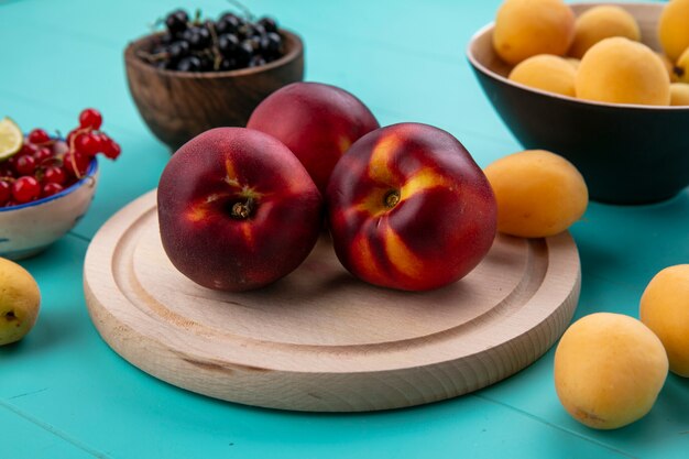 Front view of peaches on a stand with red and black currants and with apricots on a blue surface