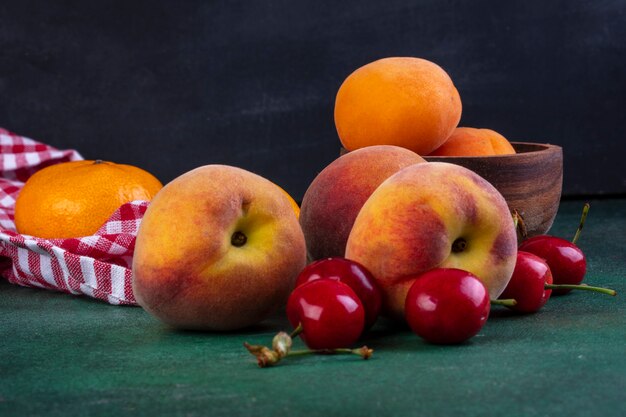 Front view peaches with cherries and apricots in a bowl on green