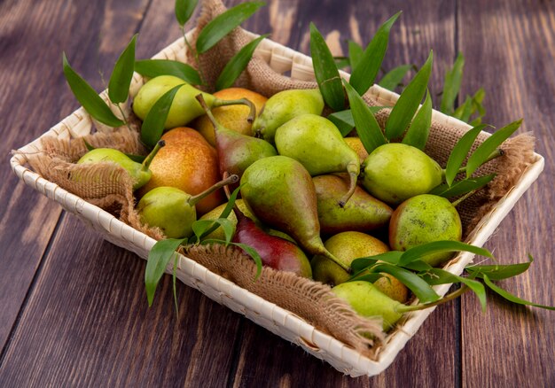 Front view of peaches with leaves in basket on wooden surface