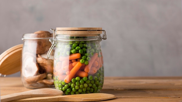 Front view of peas and baby carrots in glass jar with copy space