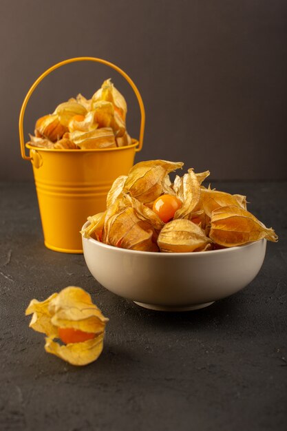 A front view peeled orange fruits inside white plate and yellow basket isolated on grey