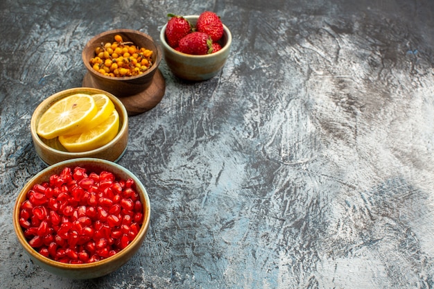 正面図は、暗い光のテーブルの色の新鮮な果物に他の果物と一緒に皮をむいたザクロ