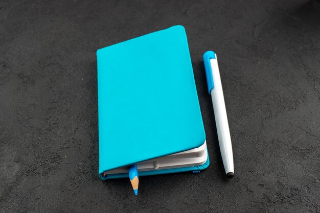 Вид спереди ручки внутри закрытой синей записной книжки и ручки на черном