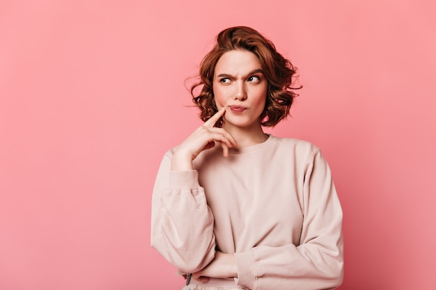 Front view of pensive pretty woman. Curly girl thinking on pink background.