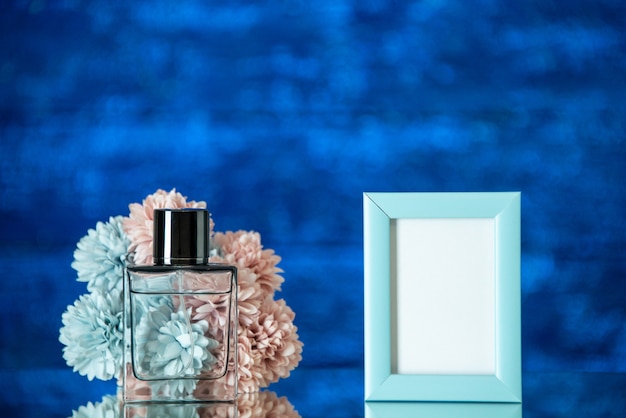 Front view perfume bottle small blue photo frame flowers on blue blurred background