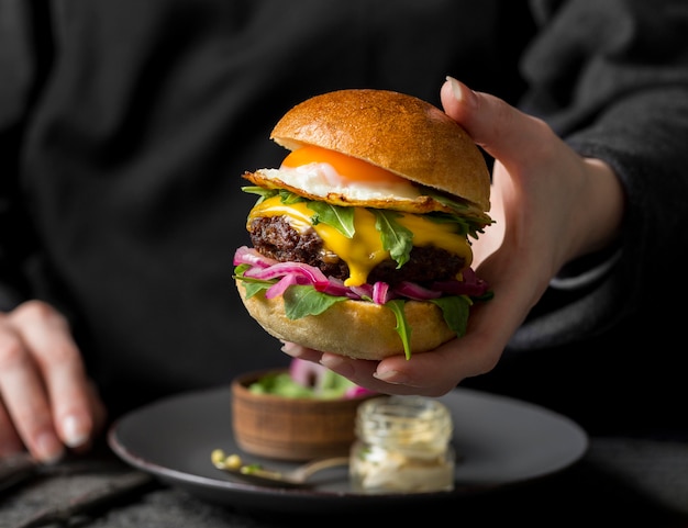 Free photo front view person holding burger with fried egg