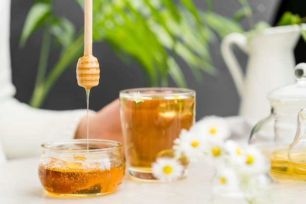 Front view person holding glass with tea and honey dipper