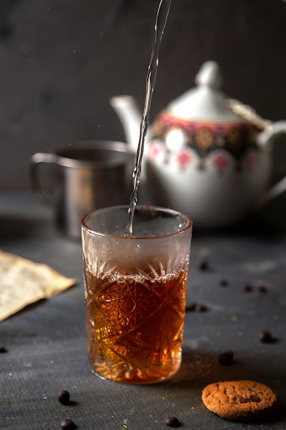 Человек вида спереди заваривает чай с кипяченой водой вместе с печеньем на темном столе, печенье, чай, печенье, сладкое