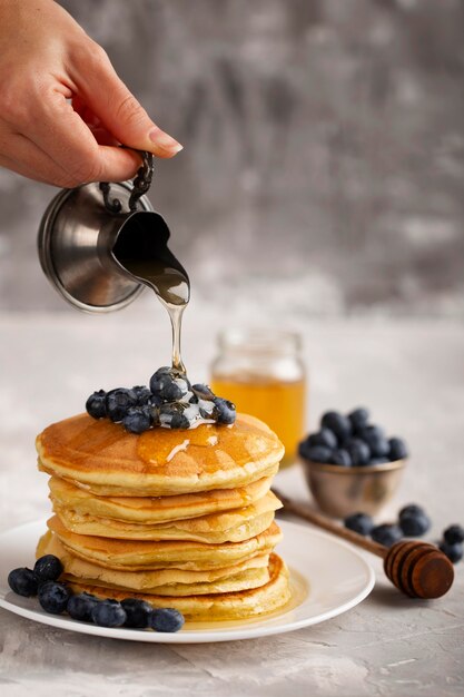 Front view person pouring maple syrop on pancakes