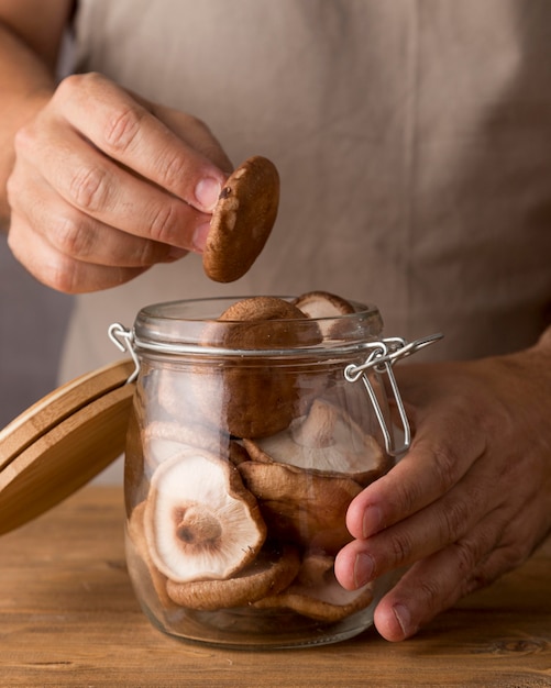 Front view of person putting mushrooms in glass jar