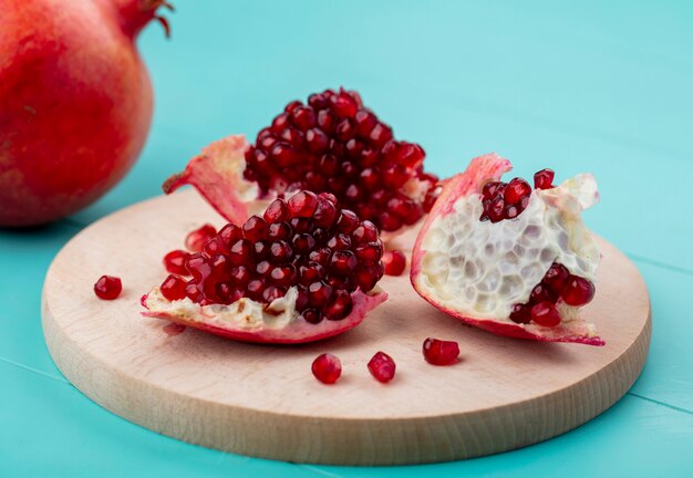 Front view of pieces of pomegranate on a cutting board on a blue surface