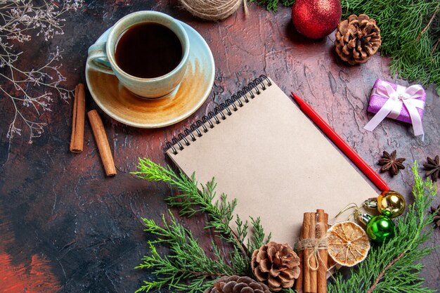 Front view pine tree branches and pinecones on a notebook red pen dried lemon slices straw thread on dark red background