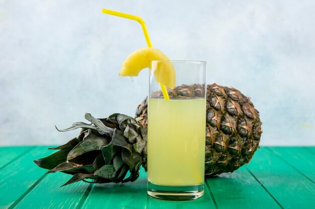 Front view of pineapple juice with pineapple on green surface and white surface