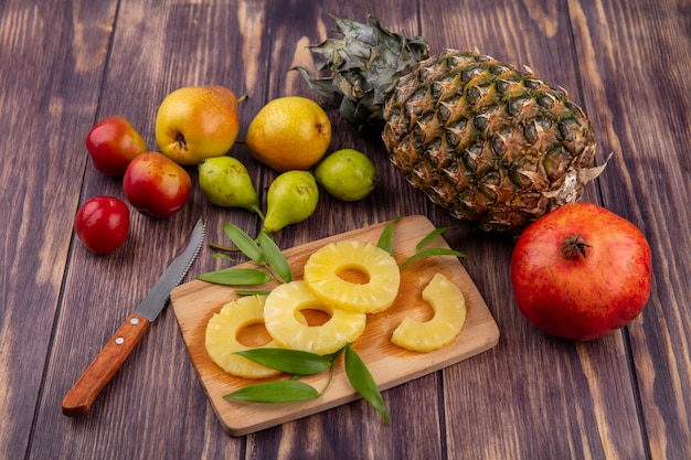 Foto gratuita vista frontale delle fette di ananas sul tagliere e ananas prugna di pesca di melograno con coltello su superficie verde