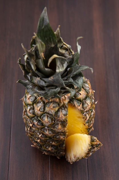 Front view of pineapple with one piece cut out from whole fruit on wooden surface