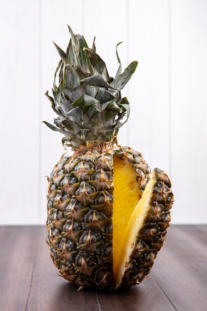 Front view of pineapple with one piece cut out from whole fruit on wooden surface