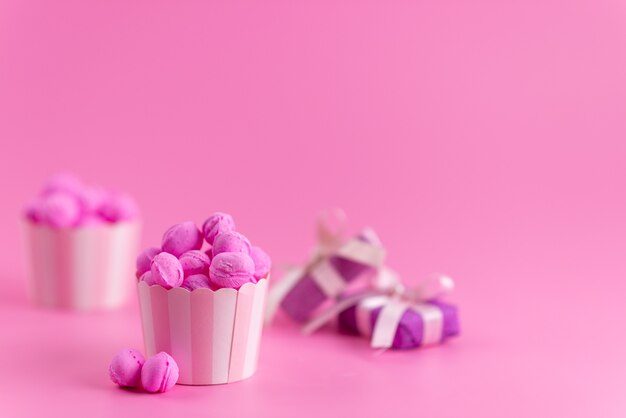 A front view pink, candies along with purple gift boxes on pink, candy color sugar sweet