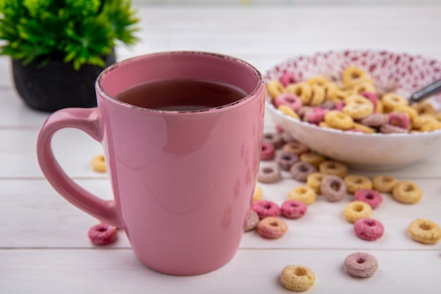 Вид спереди розовой чашки чая с хлопьями на миску на белой поверхности