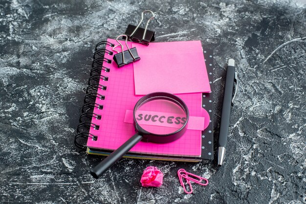 正面図ピンクのメモ帳、ペン拡大鏡、灰色の背景に成功メモ