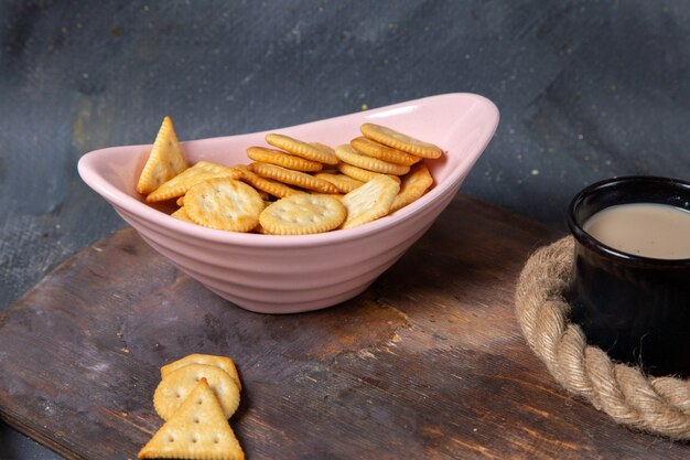 Front view pink plate with salted crackers and cup of milk on grey