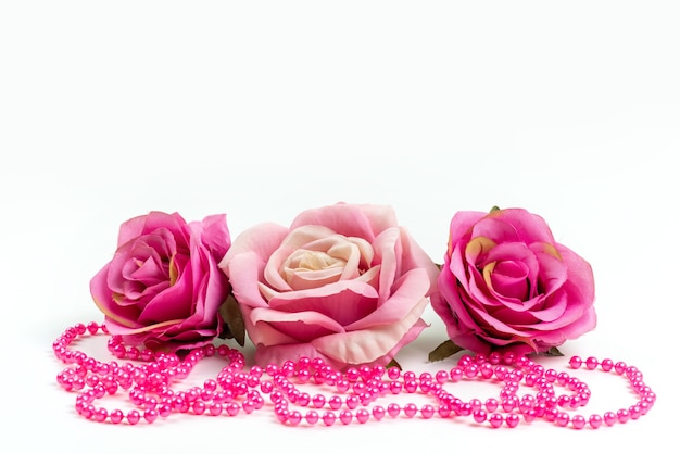 A front view pink roses along with pink necklace on white desk