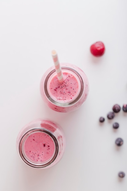 Free photo front view pink smoothie bottles with straw and berries