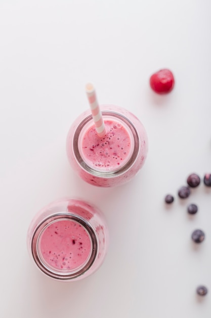 Foto gratuita vista frontale bottiglie di frullato rosa con paglia e frutti di bosco