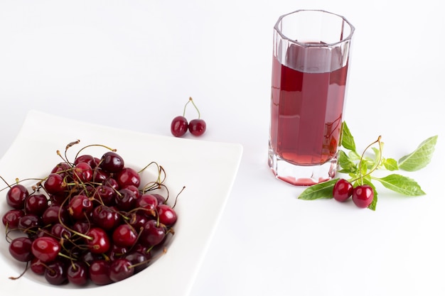 Бесплатное фото Тарелка переднего вида с вишней кислой и мягкой вместе с листьями вишневого сока на белом