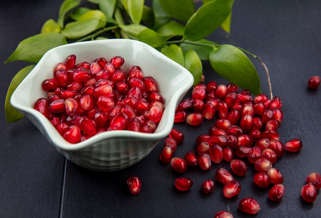 Front view of pomegranate berries in bowl and leaves on black surface