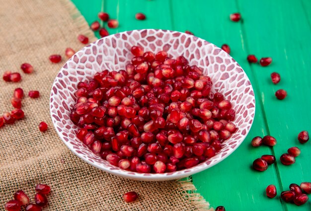 Front view of pomegranate berries in plate and on sackcloth and green surface