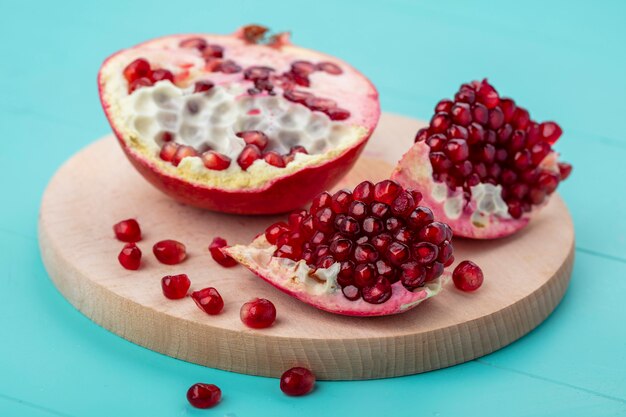 Front view of pomegranate pieces and berries with pomegranate half on cutting board on blue surface