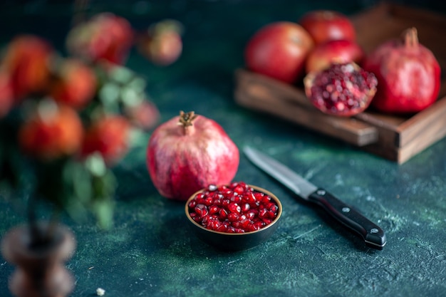 Free photo front view pomegranate seeds bowl knife pomegranates on wood board on dark surface