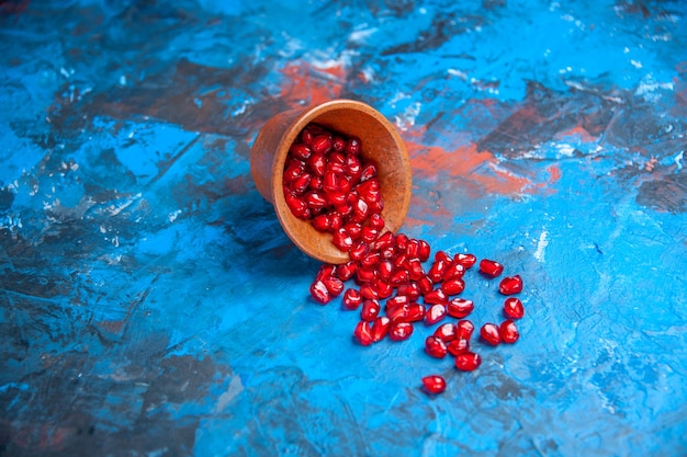 Front view pomegranate seeds in little wooden bowl on blue free place