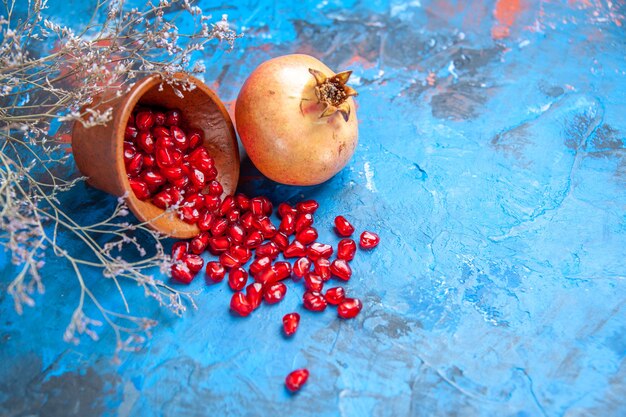 Front view pomegranate seeds in wooden bowl a pomegranate dried wild flower branch on blue free place