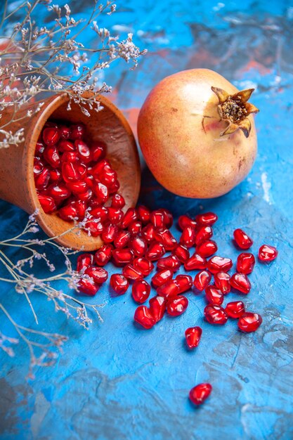 Front view pomegranate seeds in wooden bowl a pomegranate dried wild flower branch on blue