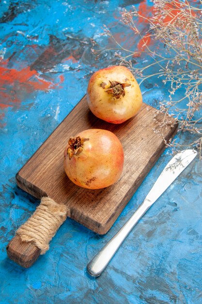 Front view pomegranates on chopping board dinner knife on blue