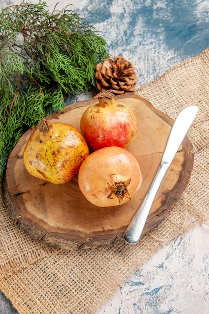 Coltello da pranzo per melograni vista frontale su albero rotondo tagliere di legno ramo di pino su sfondo blu-bianco