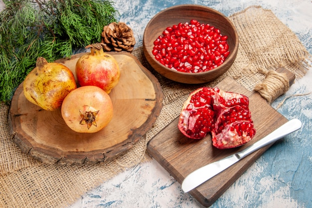 Front view pomegranates on round cutting board pomegranate seeds in bowl a cut pomegranate