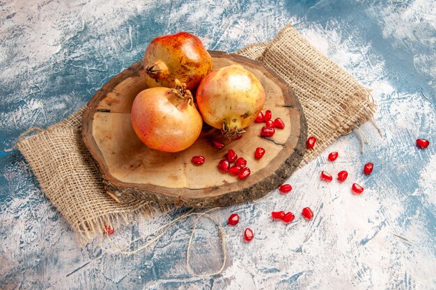 Front view pomegranates on round cutting board scattered pomegranate seeds on blue-white
