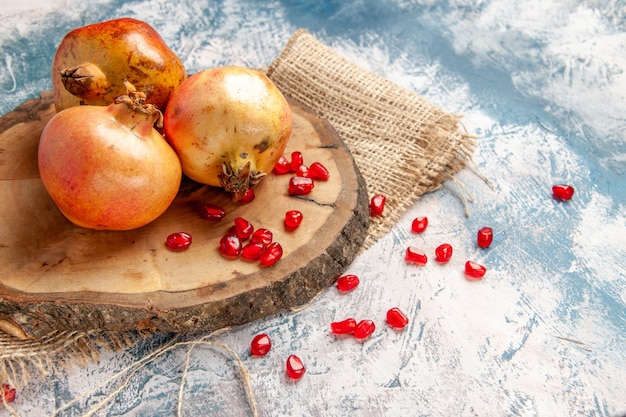 Front view pomegranates on round cutting board scattered pomegranate seeds on blue-white