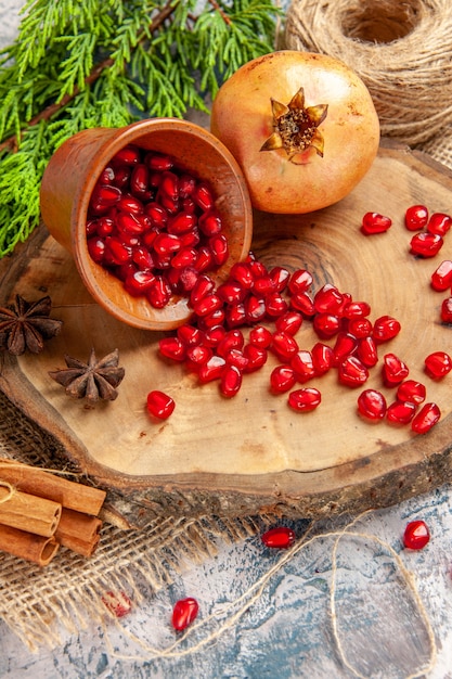 Free photo front view pomegranates scattered pomegranate seeds in bowl anise seeds on tree wood board straw thread cinnamon on blue-white background