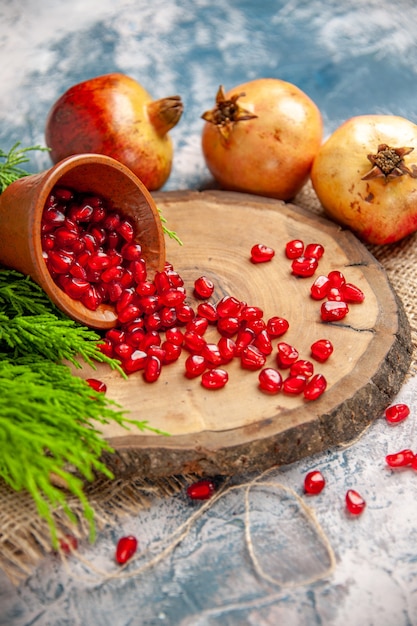 Front view pomegranates scattered pomegranate seeds in bowl on tree wood board on blue isolated background