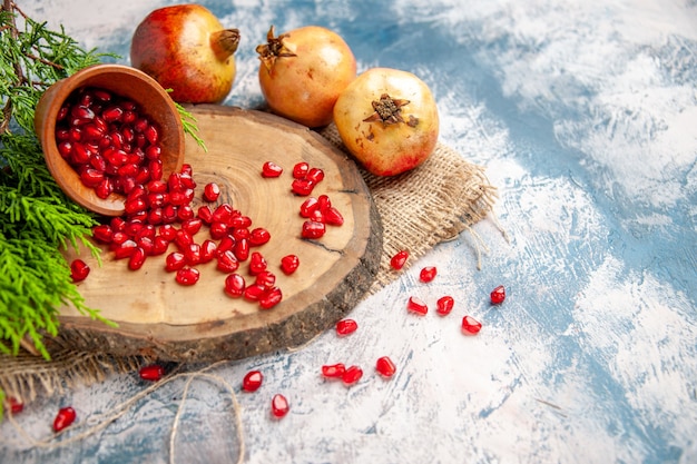 Front view pomegranates scattered pomegranate seeds in wooden bowl on round cutting board on blue-white free place